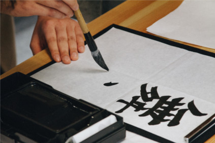 Person writing Japanese kanji with a brush